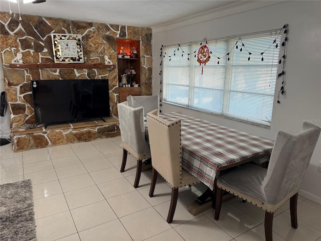 tiled dining space with crown molding and a stone fireplace