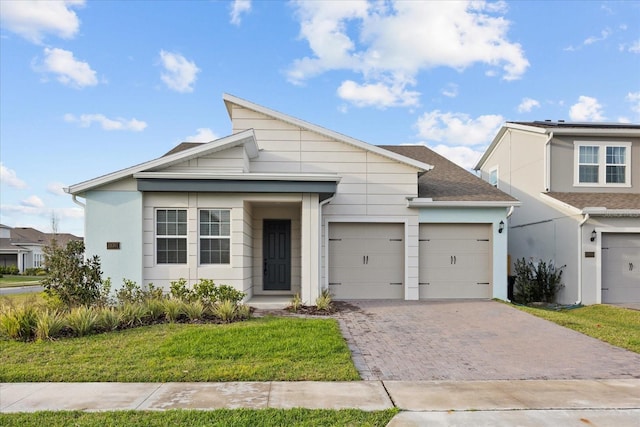 view of front facade with an attached garage, a shingled roof, decorative driveway, stucco siding, and a front lawn