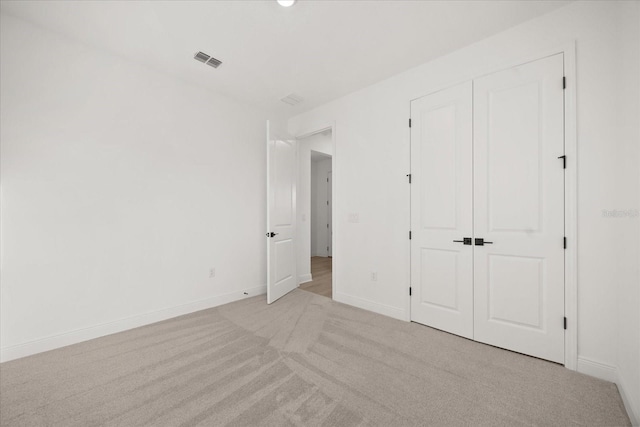 unfurnished bedroom with a closet, visible vents, light carpet, and baseboards