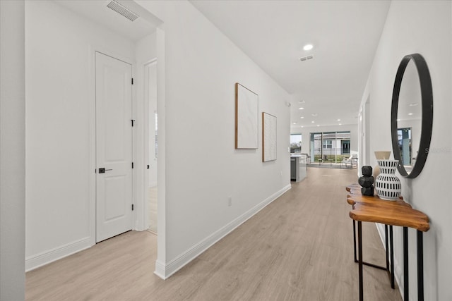 hallway with light wood-style floors, baseboards, and visible vents