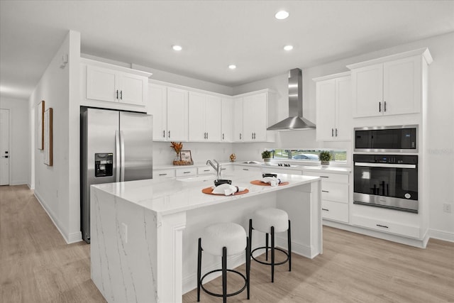 kitchen featuring appliances with stainless steel finishes, white cabinetry, a sink, wall chimney range hood, and an island with sink