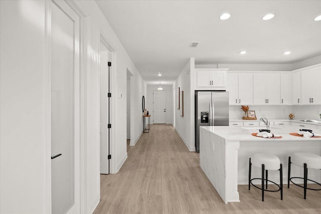 kitchen featuring recessed lighting, white cabinetry, a kitchen breakfast bar, light wood-style floors, and stainless steel fridge