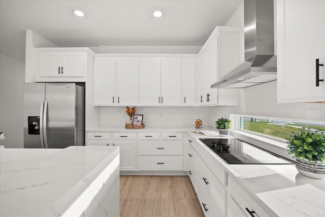 kitchen with black electric stovetop, wall chimney exhaust hood, white cabinetry, and stainless steel fridge