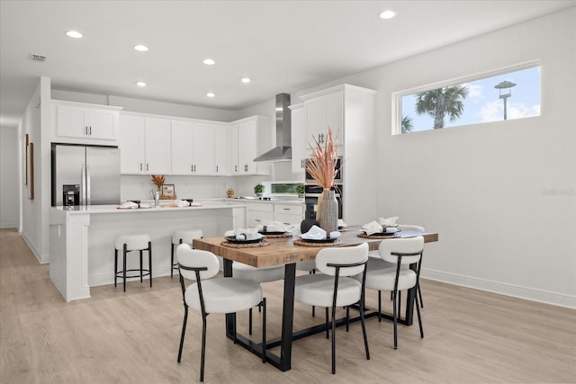 kitchen with visible vents, stainless steel refrigerator with ice dispenser, light wood finished floors, and wall chimney range hood