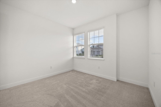 spare room featuring light colored carpet and baseboards