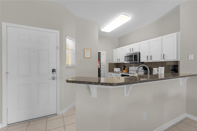 kitchen featuring stainless steel microwave, electric range, light tile patterned flooring, dark stone counters, and a kitchen bar