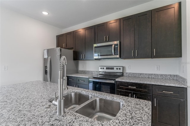 kitchen with light stone countertops, appliances with stainless steel finishes, dark brown cabinets, and a sink