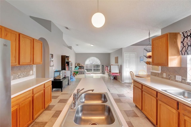 kitchen featuring lofted ceiling, a sink, open floor plan, light countertops, and freestanding refrigerator