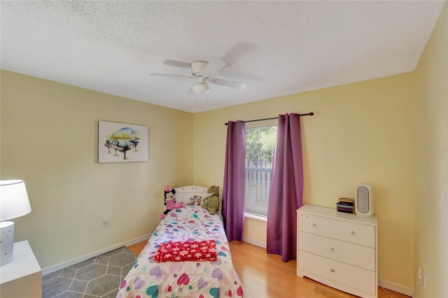 bedroom featuring a textured ceiling, light wood-style floors, a ceiling fan, and baseboards