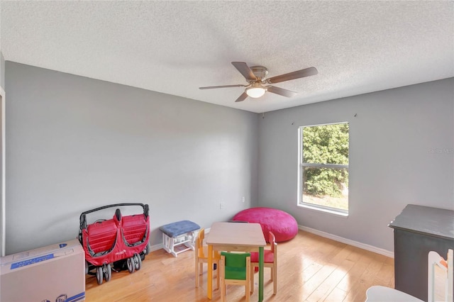 game room with ceiling fan, a textured ceiling, baseboards, and hardwood / wood-style flooring