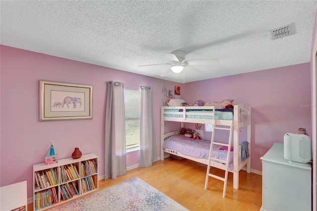 bedroom with baseboards, visible vents, ceiling fan, wood finished floors, and a textured ceiling