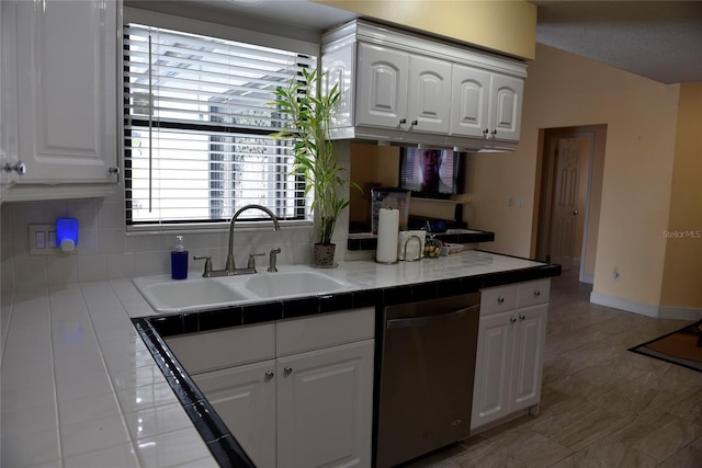 kitchen with a sink, white cabinetry, stainless steel dishwasher, and tile counters