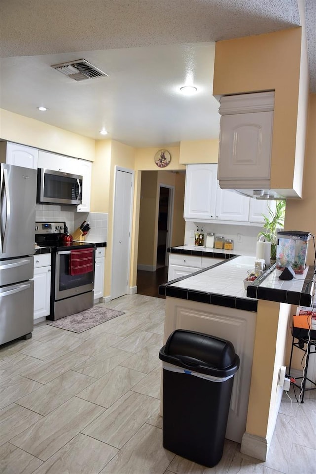 kitchen with visible vents, a peninsula, tile counters, white cabinets, and appliances with stainless steel finishes