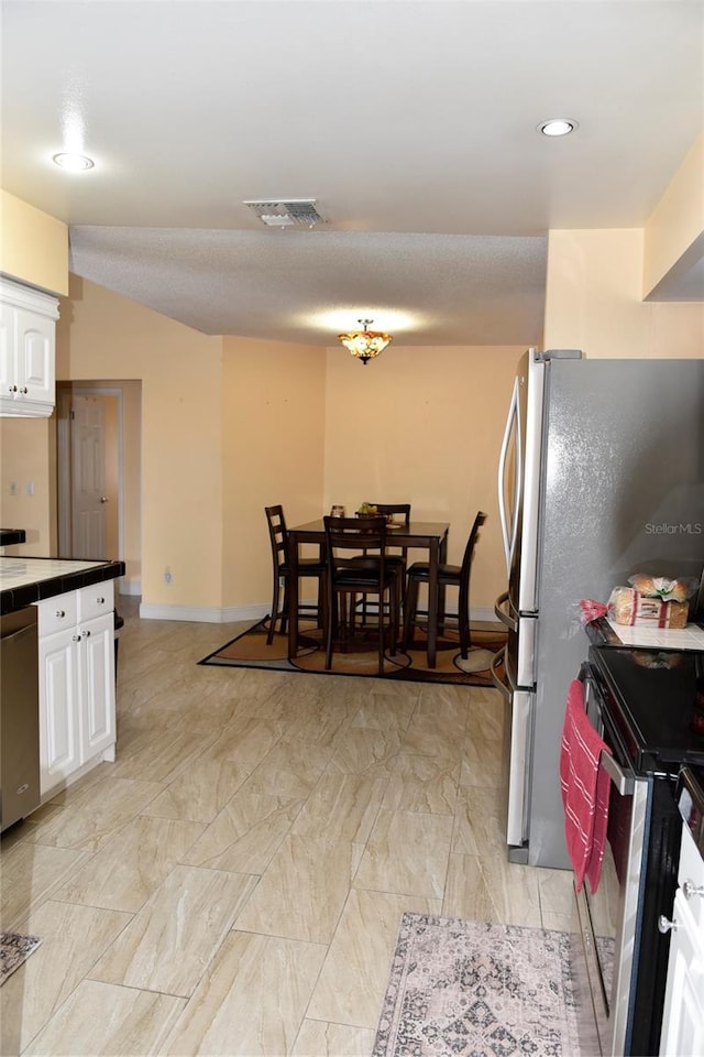 kitchen with visible vents, baseboards, tile counters, appliances with stainless steel finishes, and white cabinets