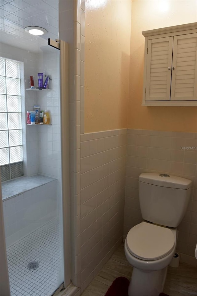 bathroom featuring a tile shower, toilet, and tile walls