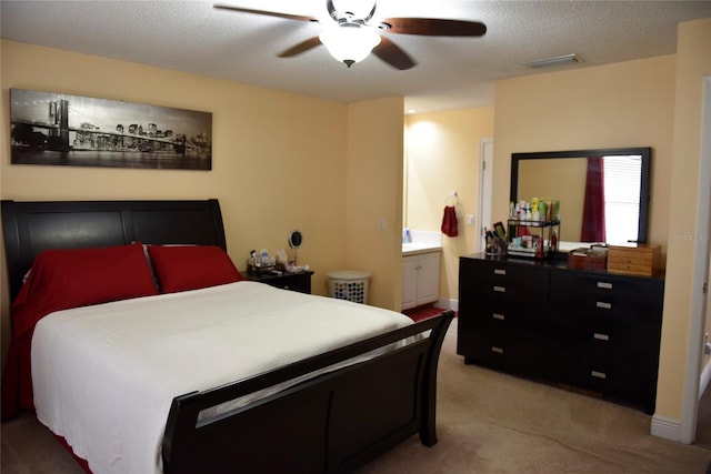 bedroom with a ceiling fan, visible vents, ensuite bathroom, a textured ceiling, and light carpet