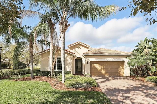 mediterranean / spanish-style home featuring a garage, stucco siding, a tiled roof, decorative driveway, and a front yard