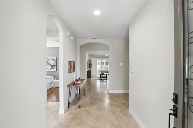 hall featuring arched walkways, baseboards, and light tile patterned floors