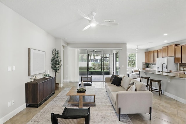 living area featuring light tile patterned floors, ceiling fan, baseboards, and a textured ceiling