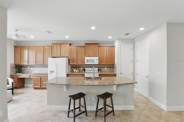 kitchen with a kitchen island with sink, white appliances, visible vents, and light stone countertops