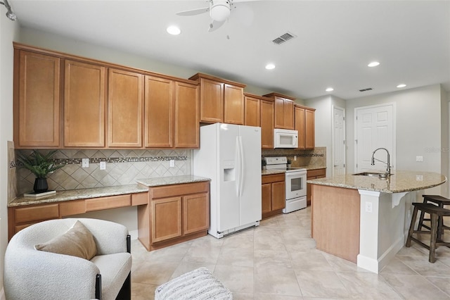 kitchen featuring light stone counters, white appliances, a sink, visible vents, and a kitchen bar