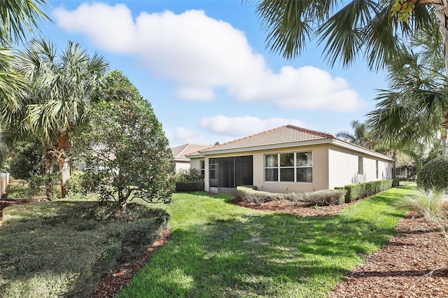 back of house featuring a tile roof, a lawn, and stucco siding