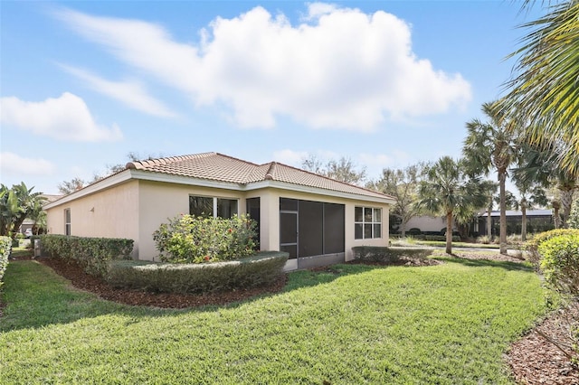 back of property with a sunroom, a tile roof, a lawn, and stucco siding