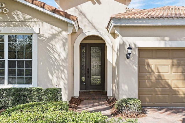 doorway to property featuring a garage, a tile roof, and stucco siding