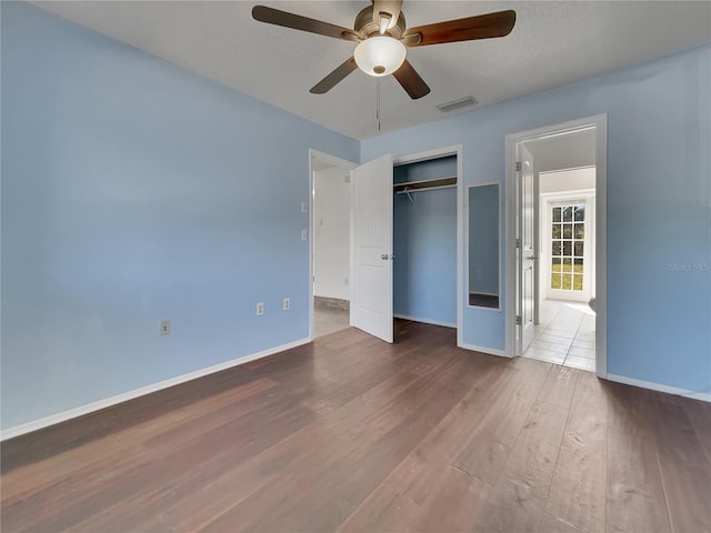 unfurnished bedroom featuring ceiling fan, wood finished floors, visible vents, baseboards, and a closet