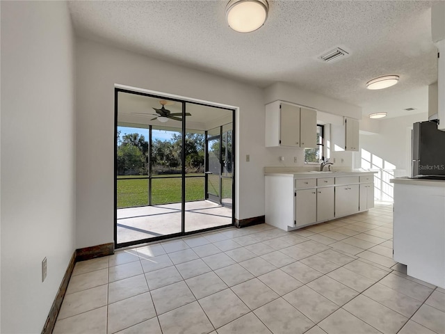 kitchen with light tile patterned floors, visible vents, white cabinetry, light countertops, and freestanding refrigerator