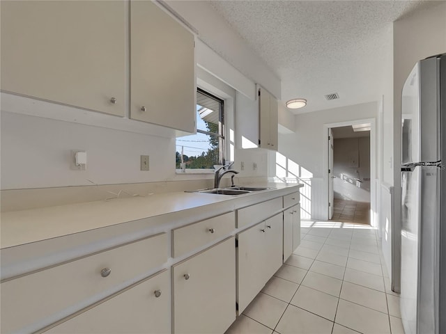 kitchen featuring light countertops, freestanding refrigerator, light tile patterned flooring, a sink, and a textured ceiling