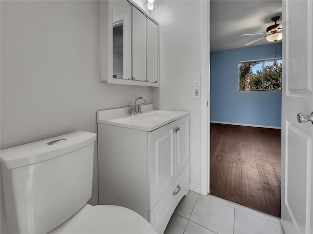 half bathroom with toilet, tile patterned flooring, a ceiling fan, and vanity