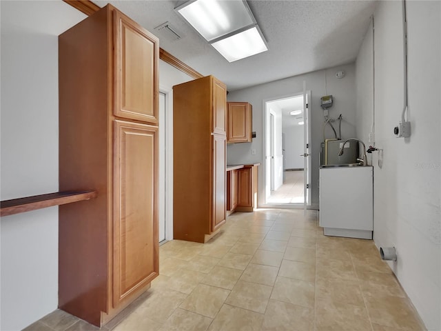 kitchen featuring light tile patterned floors, a textured ceiling, a sink, visible vents, and brown cabinetry