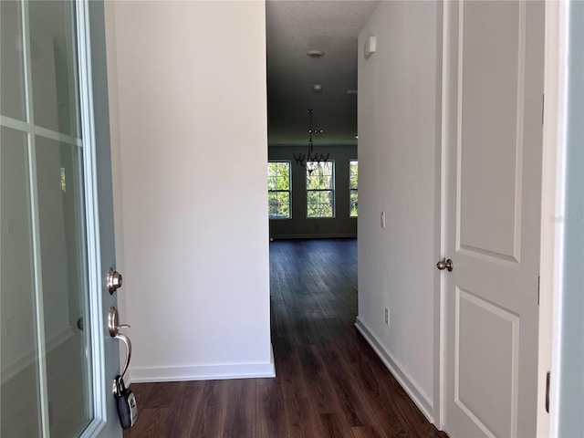 corridor featuring dark wood-style floors, baseboards, and an inviting chandelier