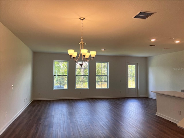 unfurnished room with a healthy amount of sunlight, an inviting chandelier, visible vents, and dark wood finished floors