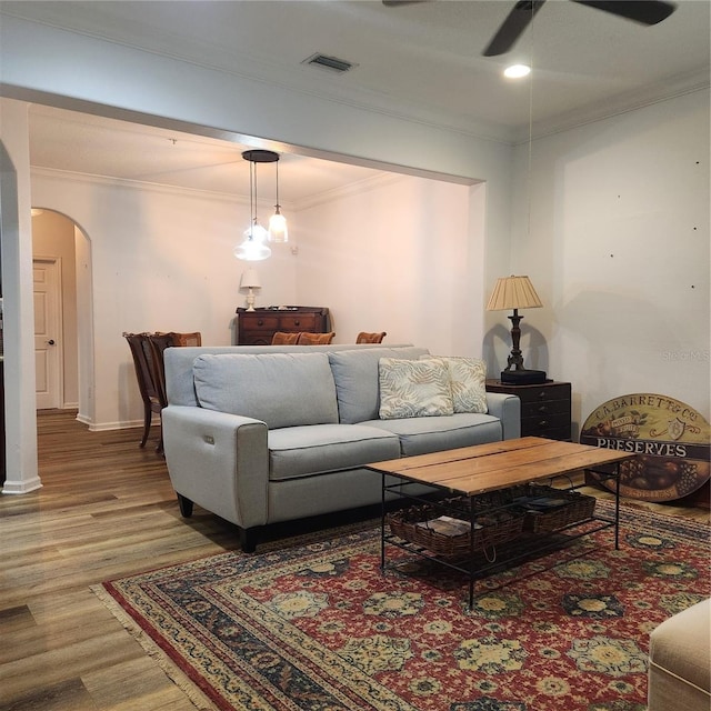 living area with arched walkways, ceiling fan, wood finished floors, visible vents, and ornamental molding