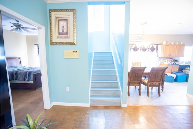 stairway with baseboards and ceiling fan with notable chandelier