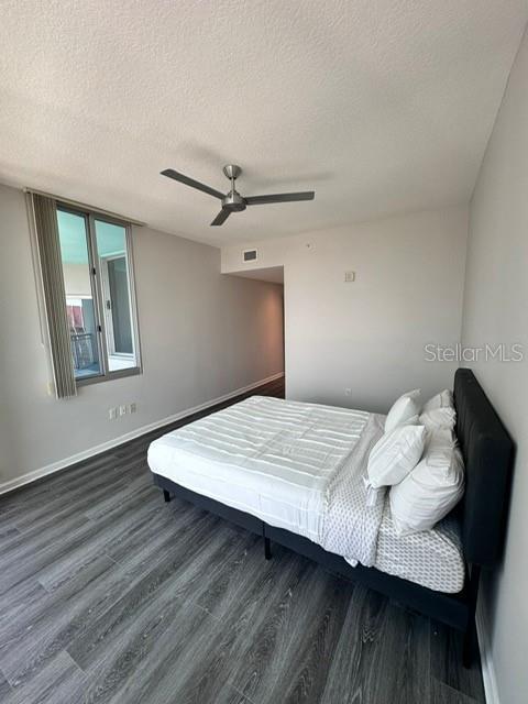 bedroom with ceiling fan, a textured ceiling, baseboards, and wood finished floors