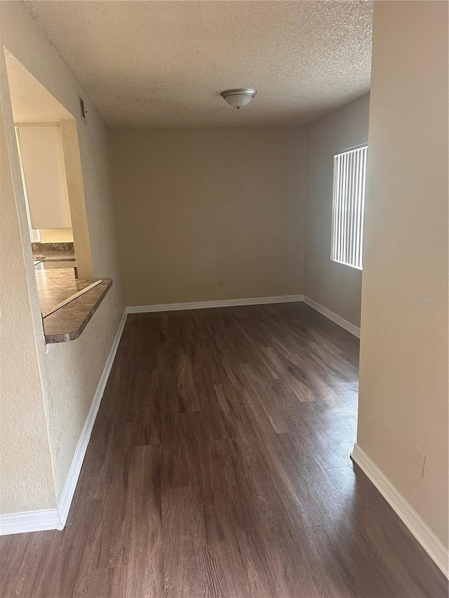 spare room featuring baseboards, a textured ceiling, and dark wood finished floors