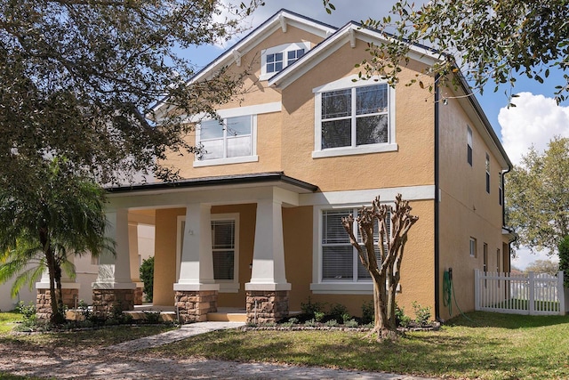 view of front of home with a porch, fence, stone siding, stucco siding, and a front yard