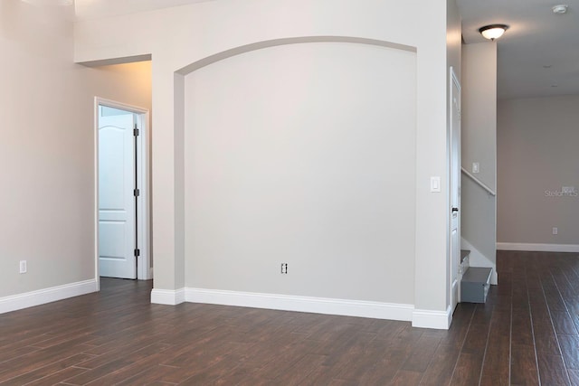 unfurnished room featuring dark wood-style floors, stairway, and baseboards