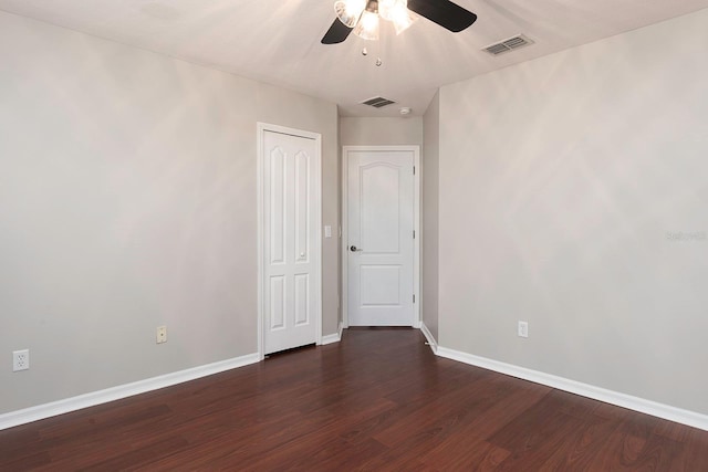 empty room with dark wood-type flooring, visible vents, ceiling fan, and baseboards