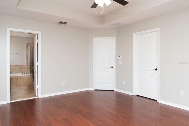 unfurnished bedroom featuring a raised ceiling, visible vents, ensuite bathroom, wood finished floors, and baseboards