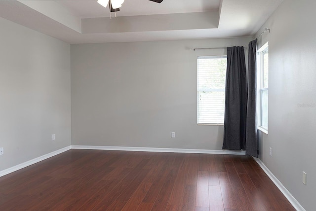 unfurnished room featuring ceiling fan, wood finished floors, a raised ceiling, and baseboards