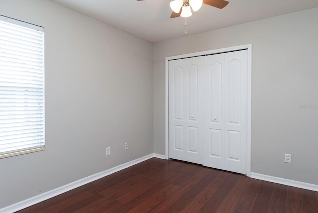 unfurnished bedroom featuring dark wood-style floors, a closet, baseboards, and a ceiling fan