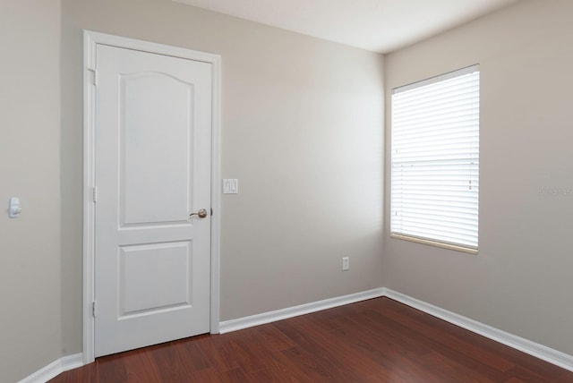 spare room with baseboards and dark wood-style flooring