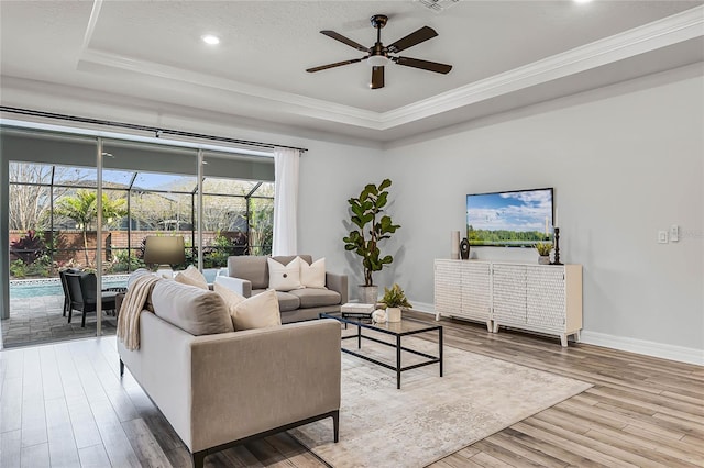 living room with a tray ceiling, wood finished floors, a sunroom, baseboards, and ceiling fan