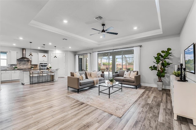 living room with a raised ceiling, light wood-style floors, visible vents, and a healthy amount of sunlight