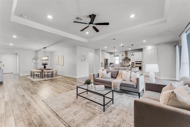 living room featuring a tray ceiling, recessed lighting, visible vents, and light wood-type flooring