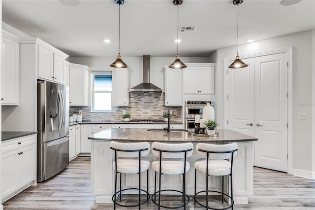 kitchen with visible vents, appliances with stainless steel finishes, light wood-type flooring, and wall chimney exhaust hood